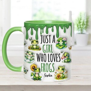 May include: A white ceramic mug with a green dripping glaze. The mug features a cartoon frog design and the text "Just a girl who loves frogs" with the name "Sophia" at the bottom.
