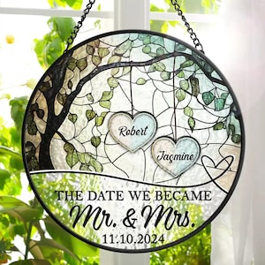 May include: A stained glass window hanging with a tree design. Two hearts hang from the branches with the names "Robert" and "Jasmine" written inside. The text "The date we became Mr. & Mrs. 11.10.2024" is written at the bottom.