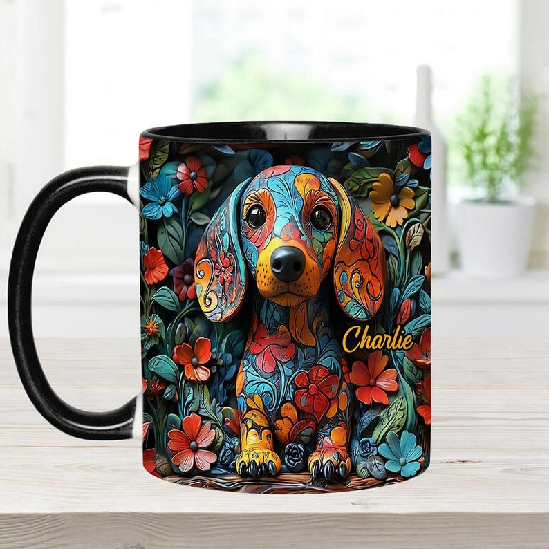 Puede incluir: Una taza de caf&eacute; negra con un dise&ntilde;o floral colorido que presenta un perro salchicha. El perro est&aacute; pintado con un patr&oacute;n vibrante azul, naranja y verde. La taza tiene un asa negra y el nombre "Charlie" est&aacute; escrito en amarillo en la taza.