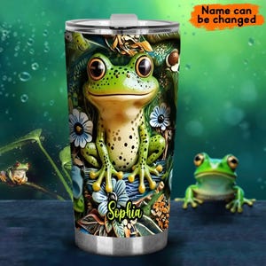 Op de afbeelding: Een roestvrijstalen tumbler met een groen kikkerontwerp. De kikker zit op een bed van groene bladeren en bloemen. De tumbler heeft een wit deksel en de naam "Sophia" staat op de zijkant gedrukt.