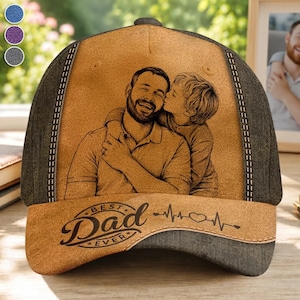 Op de afbeelding: Een beige en donkergrijze honkbalpet met een lasergegraveerde illustratie van een persoon met een baard die een kind vasthoudt. De tekst "BEST DAD EVER" staat in een cursief lettertype boven een hartslaglijn met een hartje.