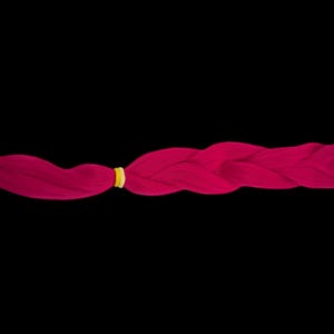 Puede incluir: Una trenza de color magenta vibrante, asegurada con una goma amarilla, sobre un fondo negro. La trenza está cuidadosamente tejida, mostrando una textura suave y un color llamativo. Este accesorio para el cabello es perfecto para añadir un toque de color.