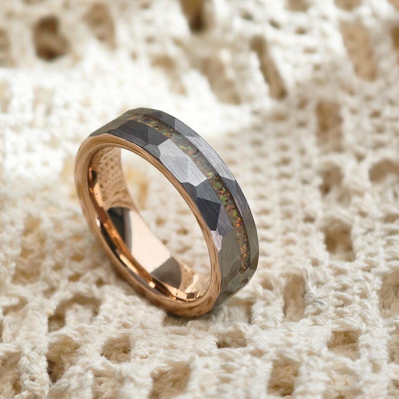 May include: A rose gold and grey ring with a faceted design. The ring has a central inlay with a speckled, iridescent appearance. The inner band of the ring is a polished rose gold colour, contrasting with the grey exterior.