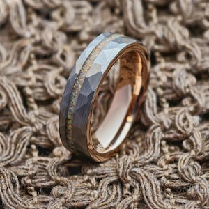 May include: A silver ring with a faceted design and an iridescent central band. The ring has a gold interior and is displayed on a textured, brown surface.