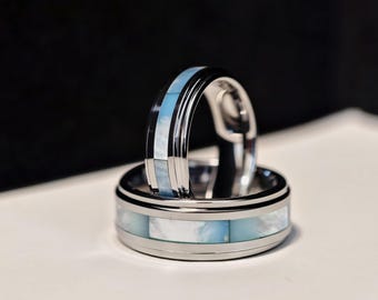 May include: Two silver wedding bands with a blue and white inlay. The bands are stacked on top of each other.