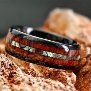 May include: A black tungsten ring with a brown wood inlay and a thin strip of abalone shell.