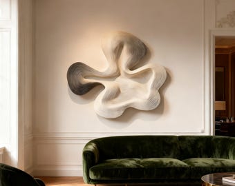May include: Abstract wall sculpture with a flowing, organic design. The artwork features a gradient of colours, transitioning from dark grey to white. It is mounted on a neutral-coloured wall above a green velvet sofa.