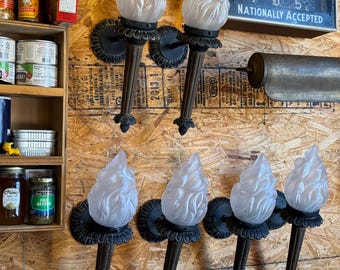 May include: Six wall-mounted torch sconces with frosted glass shades in the shape of flames. The sconces are made of dark brown metal and have a vintage style.