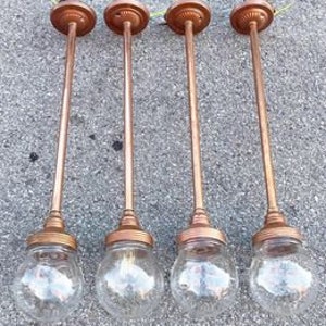 May include: Set of five copper pendant lights with clear glass shades. Each light has a long, slender stem and a decorative finial at the top.