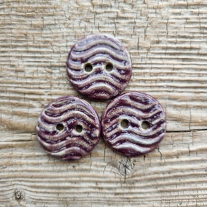 May include: Three ceramic buttons with a wavy pattern in shades of purple and white.