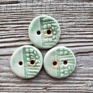 May include: Three ceramic buttons with a green and white glaze. The buttons have a textured design and two holes.