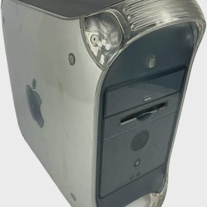 Peut inclure: Un ordinateur de bureau argenté et transparent avec une poignée. L'ordinateur a un panneau avant gris foncé avec un lecteur de CD-ROM et un haut-parleur. Le logo Apple est visible sur le côté. Le boîtier est en plastique transparent.