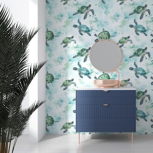 Op de afbeelding: Een badkamermeubel met een blauwe kast en een ronde spiegel. De muur achter het meubel is bedekt met behang met een aquarelpatroon van groene zeeschildpadden die zwemmen in een turquoise en witte achtergrond.