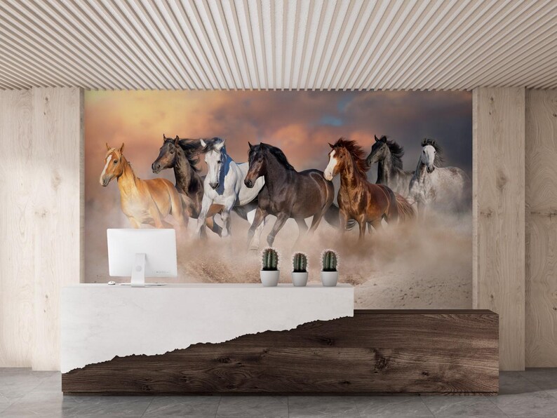 May include: A group of seven horses running through a dusty field at sunset. The horses are brown, white, and black, and they are all running in the same direction. The sky is a mix of orange, pink, and purple.