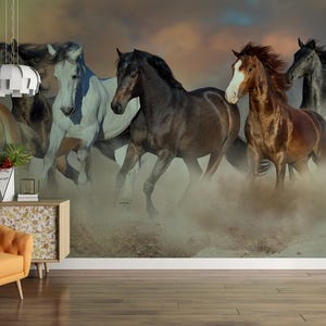 May include: A group of seven horses running through a dusty field. The horses are all different colors and breeds, and they are running in a loose formation. The background is a blurry image of a sunset.