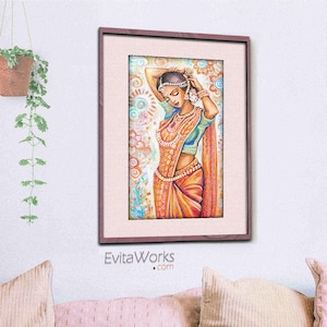 May include: Framed watercolor print of a woman in traditional Indian attire. The artwork features a woman in a colorful sari, adorned with jewelry, with her hands raised to her head. The frame is a dark wood color, and the background is a soft, patterned design.