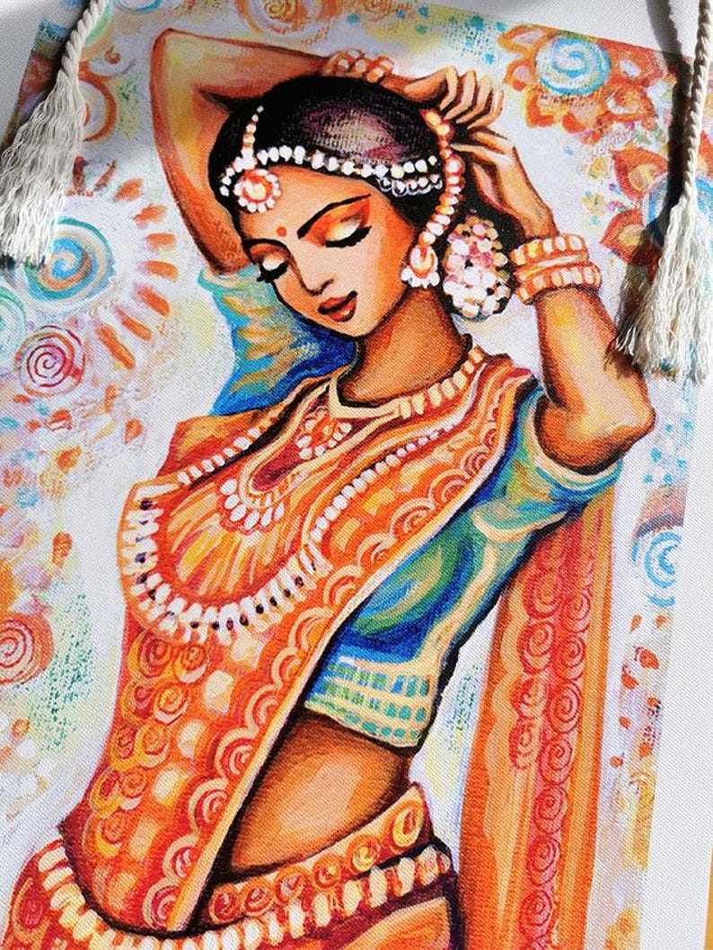 May include: A colorful painting of a woman in traditional Indian attire. The woman is adorned with jewelry and a headpiece, with her eyes closed. The artwork features vibrant orange, blue, and white hues, with decorative tassels on the sides.