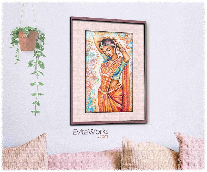 May include: Framed watercolor print of a woman in traditional Indian attire. The artwork features a woman in a colorful sari, adorned with jewelry, with her hands raised to her head. The frame is a dark wood color, and the background is a soft, patterned design.