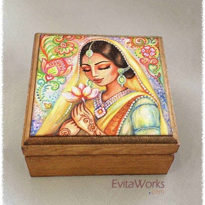 May include: A wooden box with a colourful painted lid depicting a woman in a yellow and blue sari holding a pink lotus flower. The background is a vibrant mix of floral and paisley patterns.
