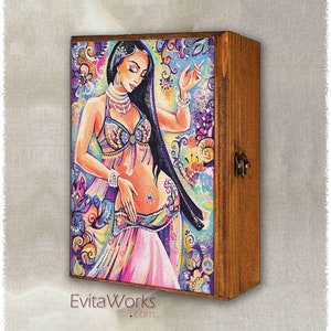 Könnte beinhalten: Eine Holzkiste mit einem Scharnierdeckel, die ein farbenfrohes Gemälde einer Frau in einem rosa und violetten Outfit mit einem floralen Hintergrund zeigt. Die Kiste hat einen Metallverschluss und der Text "EvitaWorks.com" ist auf der Unterseite aufgedruckt.