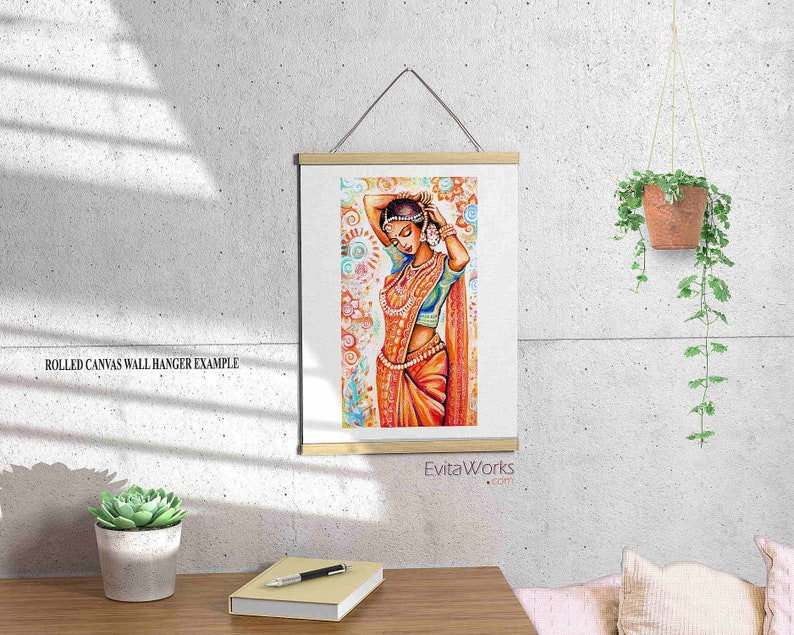 May include: A framed print of an Indian woman in traditional attire, with orange and blue tones. The artwork is displayed on a wall with a wooden frame and a hanging cord. The text "EvitaWorks.com" is visible.