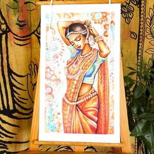 May include: An artwork depicting a woman in traditional Indian attire, adorned with jewelry and a headpiece. The artwork is displayed on a wooden easel, with a backdrop of patterned fabric. The woman is wearing a blue top and an orange sari.