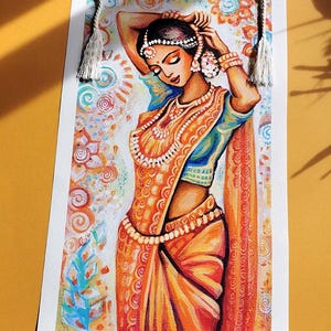 May include: A watercolor print of a woman in traditional Indian attire, featuring an orange sari with intricate patterns and jewelry. The artwork is displayed on a scroll with wooden rods and a hanging rope.