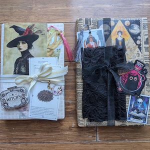 May include: Two rectangular gift-wrapped packages. The left package features a witch illustration, a small metal tin labeled Witches Powder, and a white ribbon. The right package is wrapped in newspaper print, adorned with black lace, a cat patch, and tarot cards.