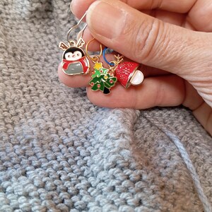 May include: Three Christmas themed stitch markers with gold rings. The markers feature a penguin, a Christmas tree, and a bell with a snowflake design.