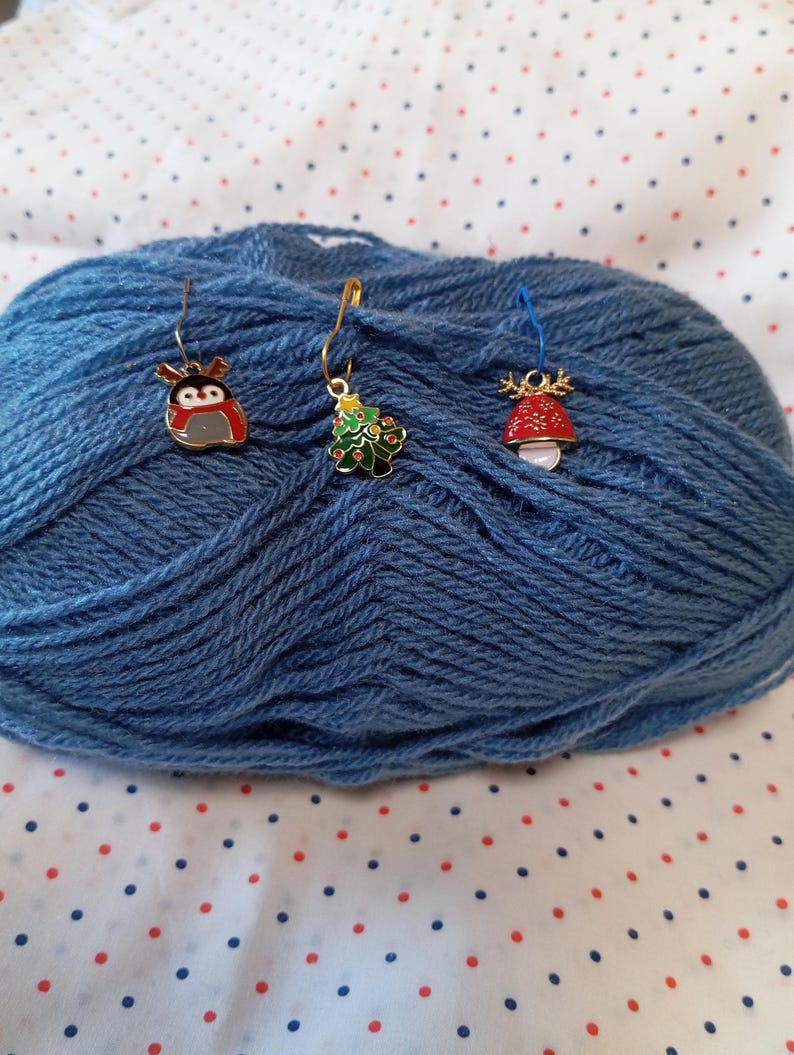 May include: Three gold metal stitch markers with different Christmas-themed charms. The charms are a penguin, a Christmas tree, and a mushroom.