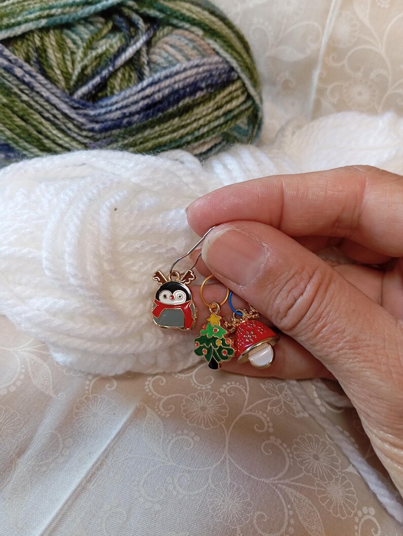May include: Three Christmas-themed stitch markers with a penguin, a Christmas tree, and a bell. The markers are gold-toned with colorful enamel details.