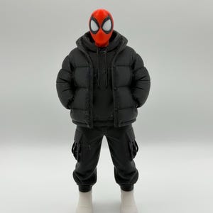 May include: A collectible action figure featuring a red mask with large white eye lenses, wearing a black hooded puffer jacket over a black hoodie, black cargo pants with side pockets, and plain white sneakers, standing in a neutral pose.