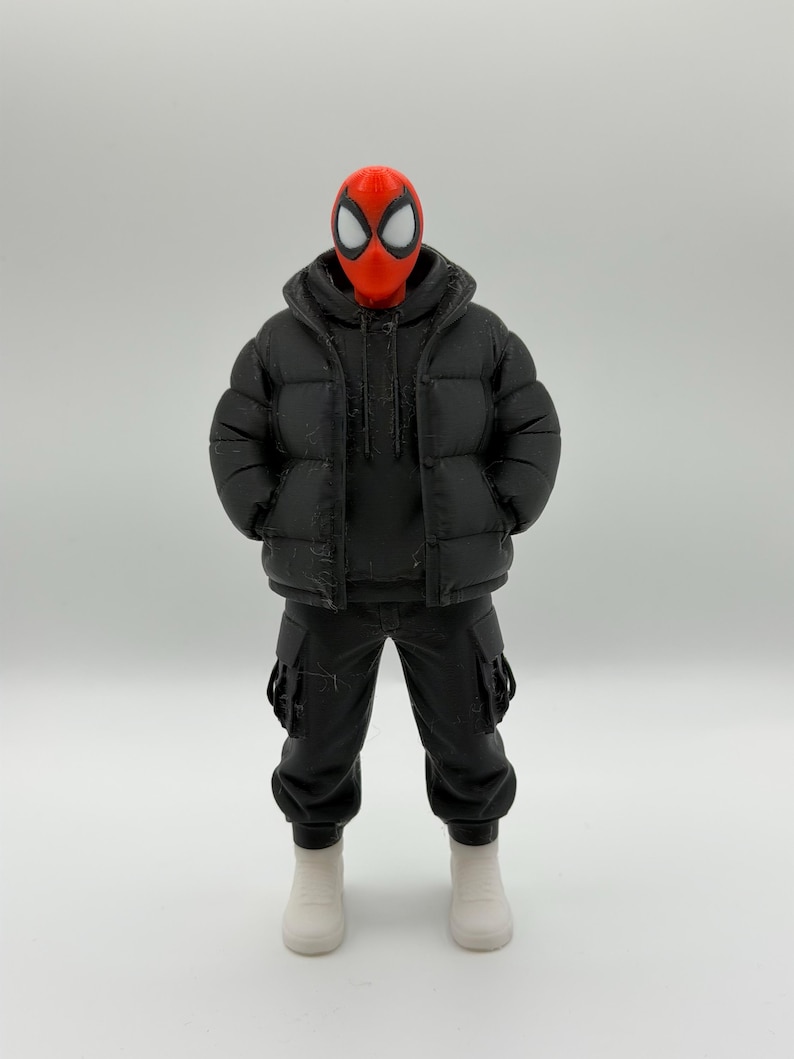 May include: A collectible action figure featuring a red mask with large white eye lenses, wearing a black hooded puffer jacket over a black hoodie, black cargo pants with side pockets, and plain white sneakers, standing in a neutral pose.