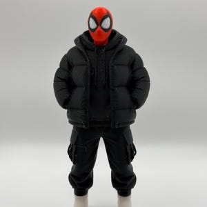May include: A collectible action figure featuring a red mask with large white eye lenses, wearing a black hooded puffer jacket over a black hoodie, black cargo pants with side pockets, and plain white boots, standing in a neutral pose.