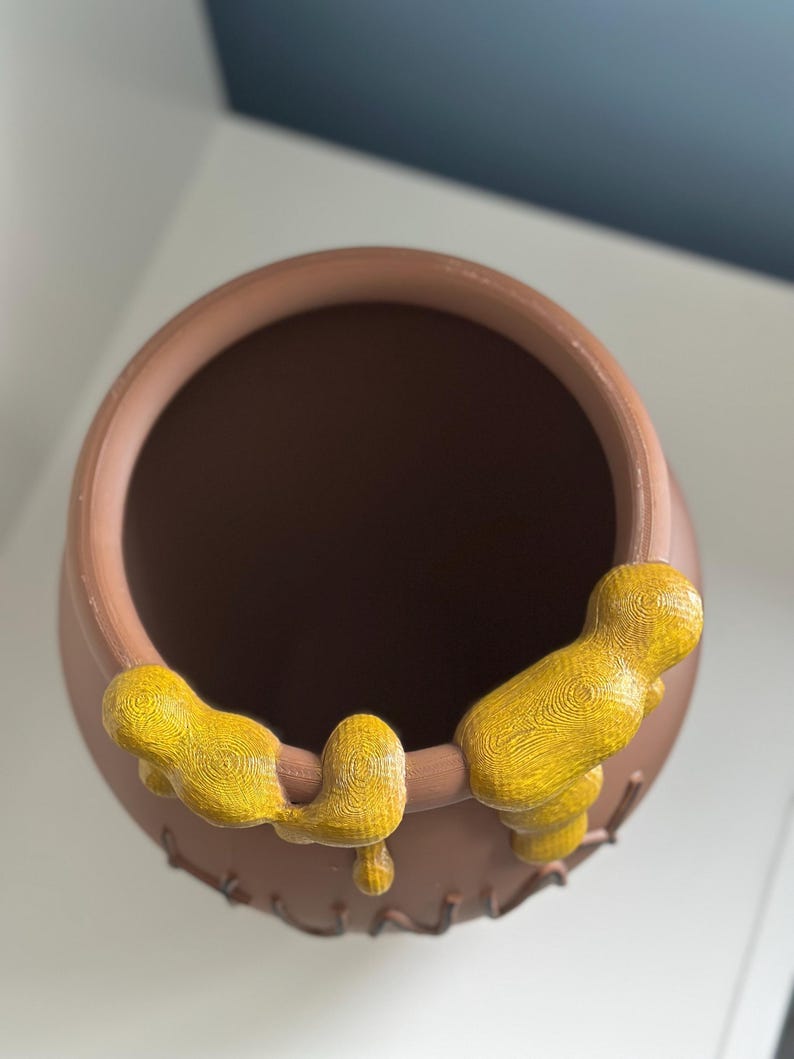 May include: A brown ceramic honey pot with a yellow honey drip design. The pot is empty and has the word "Hunny" written on the side.