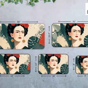 May include: Rectangular desk mats featuring a portrait of Frida Kahlo with red flowers in her hair, gold earrings, and a black dress. The mats are available in various sizes, with the largest measuring 36 inches by 18 inches.
