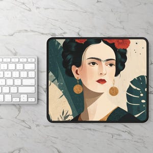 May include: Rectangular mousepad featuring a stylized portrait of Frida Kahlo with red flowers in her hair and gold earrings. The background includes tropical leaves in shades of green and beige. The mousepad has a black border.