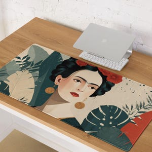 May include: A rectangular desk mat featuring a portrait of a woman with dark hair, red flowers, and gold earrings. The mat has a beige background with green and red foliage. A laptop and keyboard are on the wooden desk.