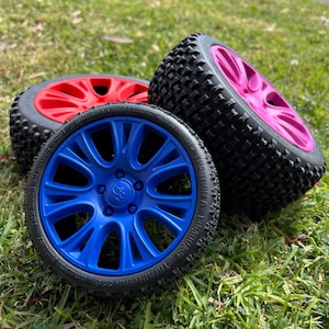 May include: Three toy car tires with different colored rims. The tires are black with a tread pattern. The rims are red, blue, and pink.
