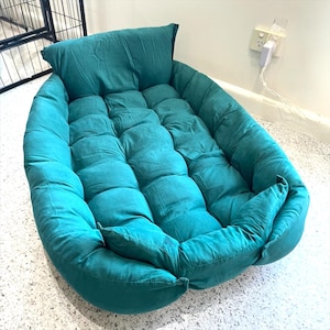 Op de afbeelding: Teal kleurig huisdierbed met een gewatteerd ontwerp. Het bed heeft een ingebouwd kussen en een zachte, pluche textuur. Het ovaalvormige bed is ontworpen voor comfort en ondersteuning, en biedt een gezellige plek voor een kleine hond of kat.