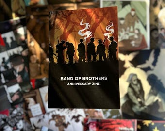 Op de afbeelding: Een Band of Brothers Anniversary Zine met een silhouetillustratie van soldaten tegen een oranje bosachtergrond met witte rook. De tekst Band of Brothers Anniversary Zine is in het wit afgedrukt.