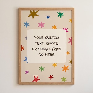 Puede incluir: Una impresión rectangular enmarcada con fondo beige claro y estrellas multicolores dispersas en tonos azul, verde, amarillo, naranja, rosa y rojo. Un bloque rectangular blanco central contiene el texto: YOUR CUSTOM TEXT, QUOTE OR SONG LYRICS GO HERE.