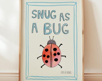 Puede incluir: Una lámina decorativa enmarcada con fondo crema claro y un borde azul dibujado a mano. El texto dice SNUG AS A BUG en letras azules, con una ilustración de una mariquita roja debajo y el pequeño texto IN A RUG en la esquina inferior derecha.