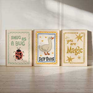 May include: Three framed art prints with whimsical illustrations. One features a ladybug with the text "Snug as a Bug." Another shows a goose with "Silly Goose." The third print has gold stars and the words "You are Magic."