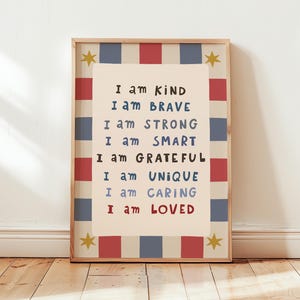 May include: A rectangular framed wall art print featuring a cream-colored center with the text: I am KIND, I am BRAVE, I am STRONG, I am SMART, I am GRATEFUL, I am UNIQUE, I am CARING, I am LOVED. The border has red and blue stripes and yellow stars.
