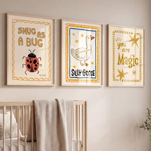 May include: Three framed art prints with whimsical illustrations. One print says "SNUG AS A BUG" with a ladybug. Another says "SILLY GOOSE" with a goose. The third says "you are Magic" with stars. The prints are in light wood frames.