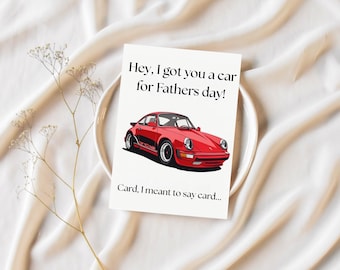 Op de afbeelding: Wenskaart voor Vaderdag met een illustratie van een rode sportwagen. De tekst op de kaart luidt: "Hey, I got you a car for Fathers day! Card, I meant to say card..." op een witte achtergrond. De kaart ligt op een witte plaat.
