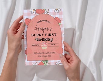 May include: A pink and white invitation card with the text "Harper's BERRY FIRST Birthday" and a cupcake illustration. The card has a strawberry and flower design and is held by two hands.