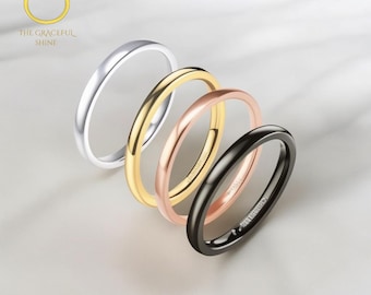 May include: Four slim rings in silver, gold, rose gold, and black are presented on a white surface. The rings are plain bands with a smooth, polished finish. The rings are slightly angled, highlighting their circular form. The logo for "The Graceful Shine" is in the upper left corner.