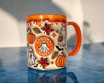 May include: A white ceramic mug with an orange rim and handle. The mug has a Halloween theme with ghosts, pumpkins, and leaves. The text "Spooky Vibes" is printed on the mug.